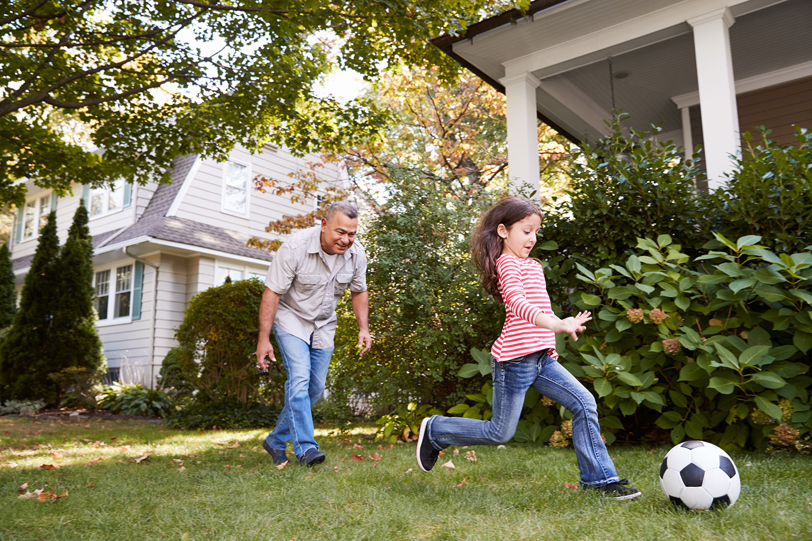 Man with girl kicking soccer ball